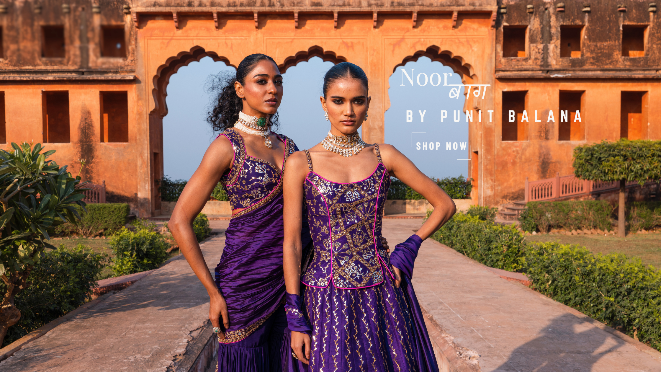 Two women in traditional purple and gold outfits standing in front of a historic building.