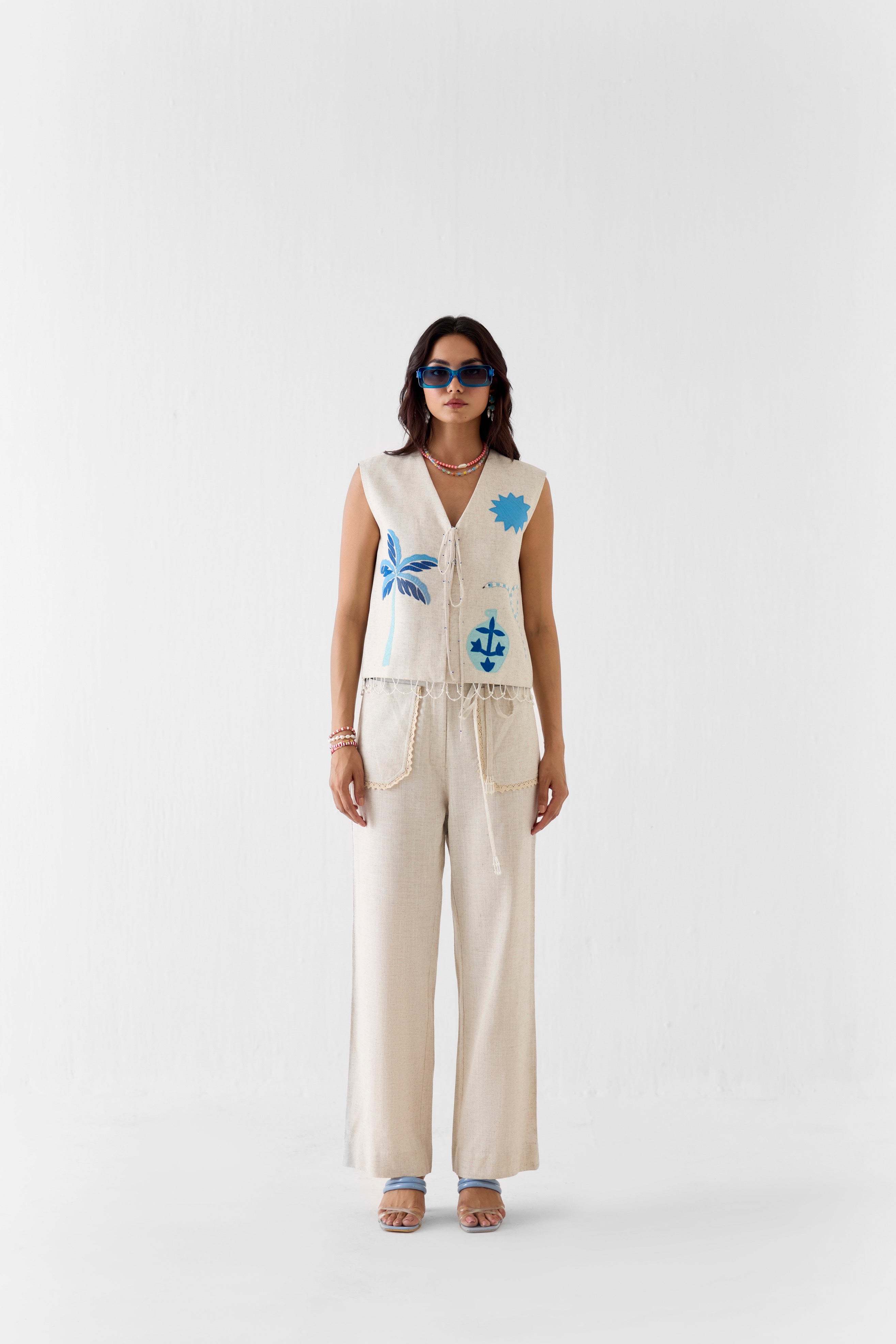 Woman wearing a sleeveless top with anchor design and beige pants on a white background