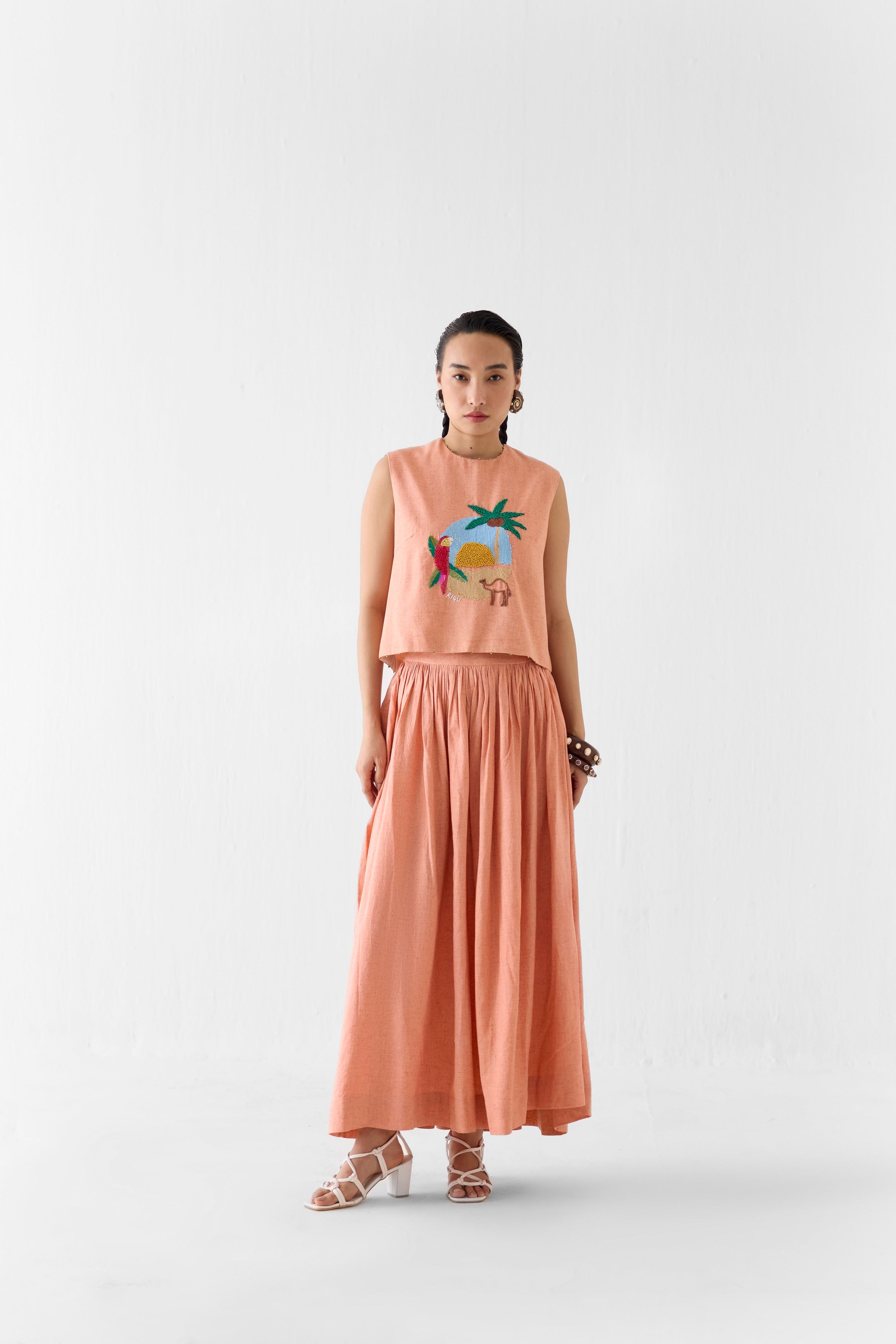 Woman wearing a peach-colored top with a graphic design and a matching skirt on a white background