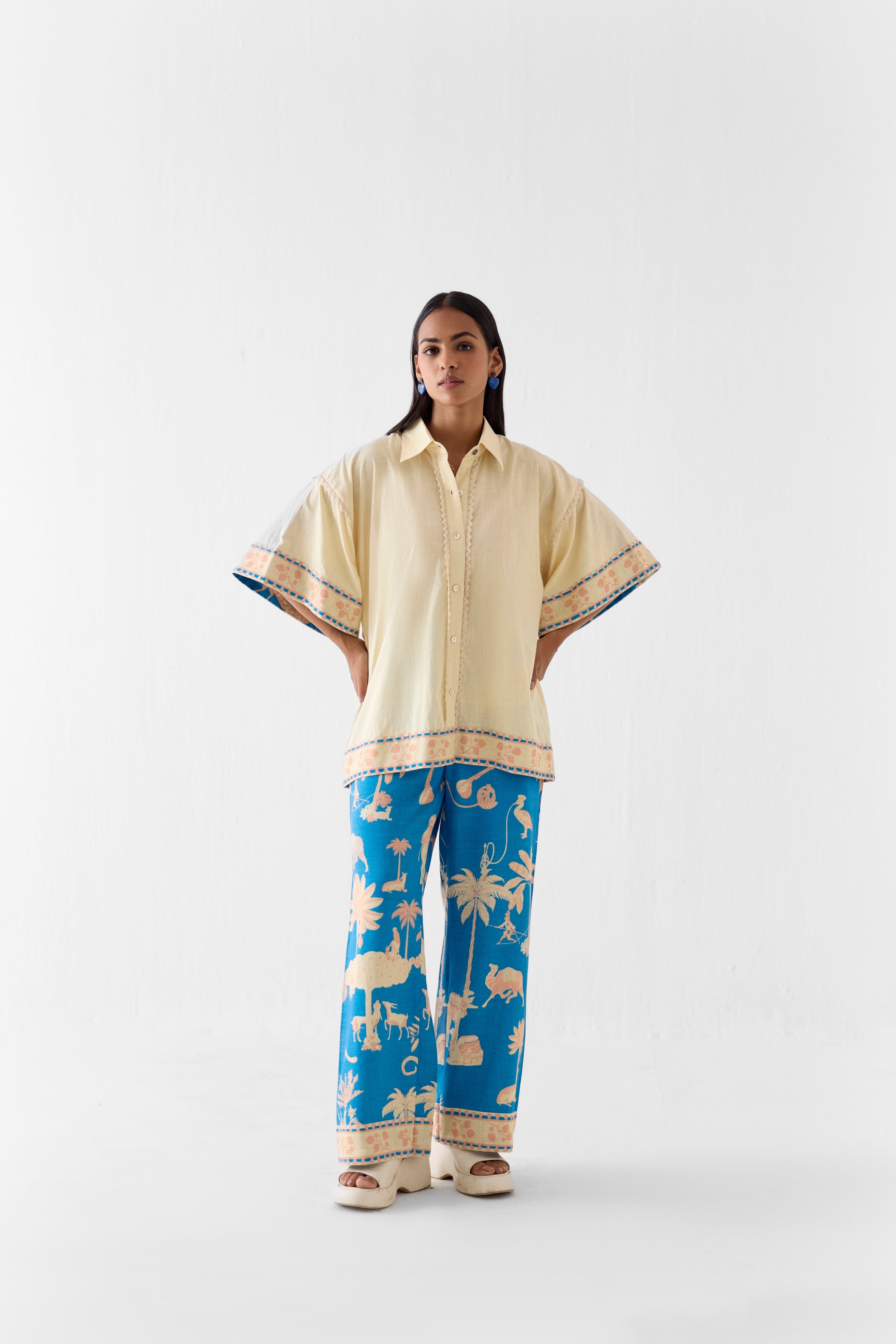 Woman wearing a beige shirt and blue patterned pants on a white background